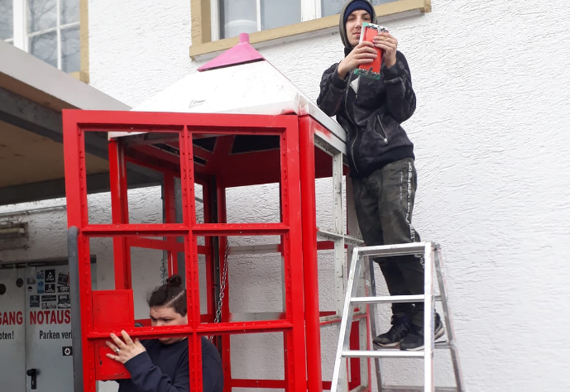 rote Telefonzelle, Jugendlicher auf der Leiter mit Handy