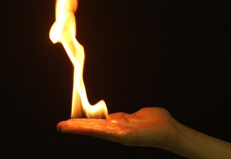 Flamme die auf einer Handfläche tanzt vor schwarzem Hintergrund